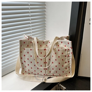 Detail of off-white corduroy tote bag featuring red heart patterns and wide shoulder strap