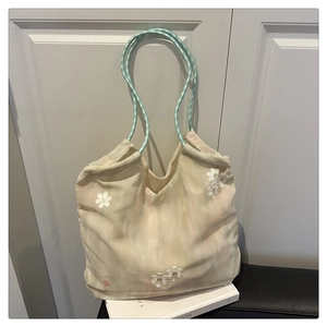 Detail of canvas tote bag with 3D daisy flowers and braided green handles in a home setting