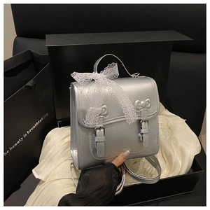 Close-up of silver backpack with white lace bow and buckles on silk background