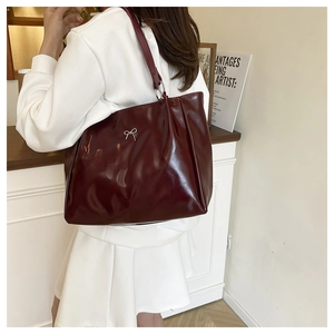 Detail of burgundy glossy leather tote bag featuring a silver bow buckle and large capacity
