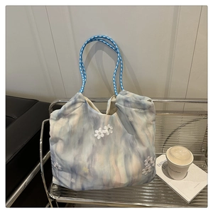 Detailed macro view of tie-dye fabric tote bag with 3D floral applique and woven handles
