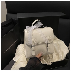 Close-up of white lace bow and embossed ribbon detail on cream PU leather backpack