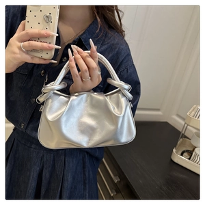 Detail of silver metallic pleated handbag with unique handle on a dark wooden surface