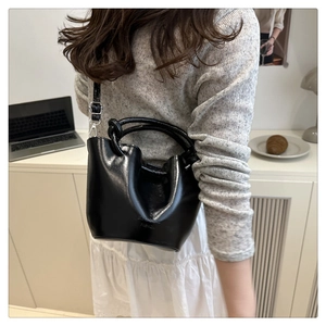 Model view of black bucket bag with pleated closure and circular handle for crossbody style