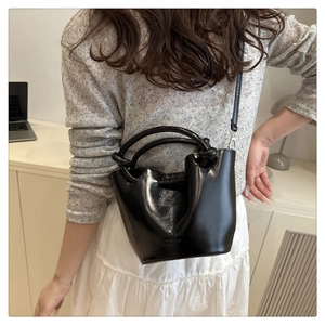 Detail of a black glossy bucket bag featuring a unique knotted handle and slim strap