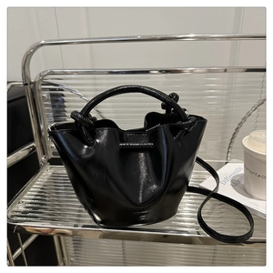 Detail of a black glossy bucket bag with metal ring handle on a modern shelf