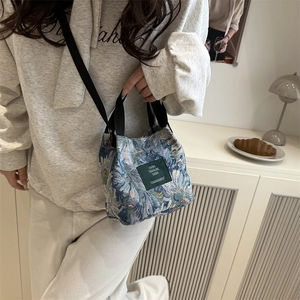 Floral bucket bag with a dark green leather patch and black crossbody nylon strap