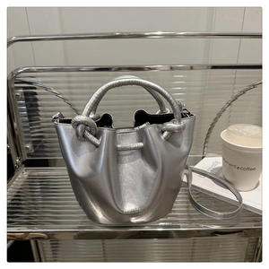 Close-up of silver leather bucket bag with a unique knotted handle and embossed logo