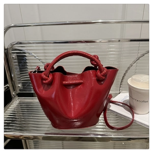 Detailed shot of a red patent leather bucket bag featuring a unique knot handle design