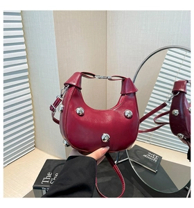 Detailed macro view of burgundy polished leather crescent bag with silver stud rivets