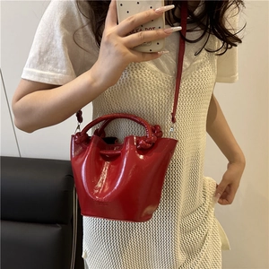 Red patent leather bucket bag with knotted handle and shoulder strap worn by a model