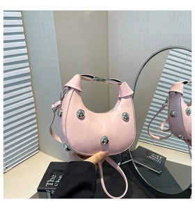 Macro detail of pink crescent leather handbag with silver stud accents and adjustable strap