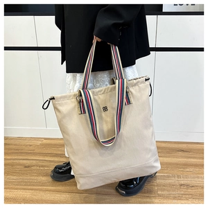 Close-up of beige canvas tote with striped handles and side drawstring detailing