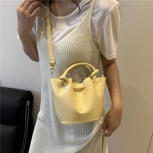 Creamy yellow glossy leather bucket bag with knotted handle and adjustable strap