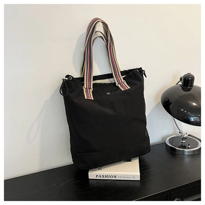 Detail of black canvas tote bag showing striped handles and adjustable side drawstrings