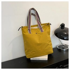 Detail of yellow canvas tote bag featuring tricolor striped handles and logo embroidery