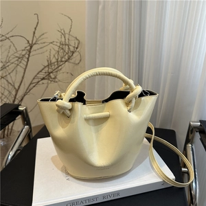 Chic pale yellow bucket bag with knotted handle and shoulder strap on a white book