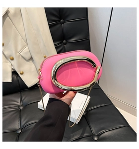 Detail of neon pink crossbody bag featuring a bold gold C-handle and metallic chain strap