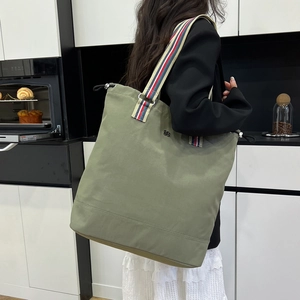 Olive green canvas tote bag with a colorful striped shoulder strap shown on a model