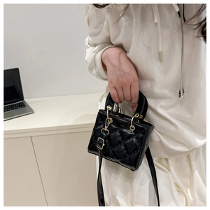 Detail of black quilted mini handbag with gold hardware and twin ring handles