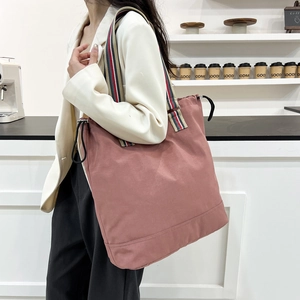 Minimalist large pink tote bag with striped handles shown on a model in a cafe setting