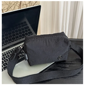 Détail du sac à bandoulière en nylon noir avec logo métallique et tissu imperméable