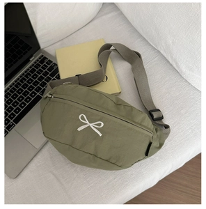 Detail der weißen Schleifenstickerei auf grüner Nylon-Halbmondtasche mit Trageriemen