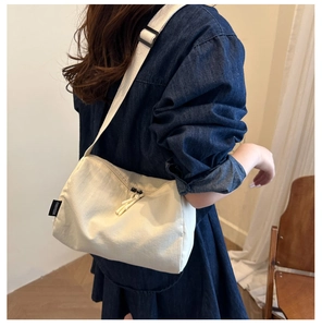 Detail of off-white canvas crossbody bag with adjustable strap and brand tag