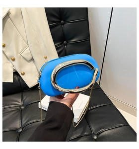 Macro detail of vibrant blue square box bag with gold C-handle on black leather sofa