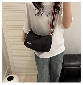 Détail d'un sac bandoulière en toile noire avec une sangle sport tricolore rayée