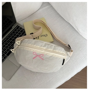 Detail einer beigen Gürteltasche mit rosa Schleifenstickerei und Schultergurt