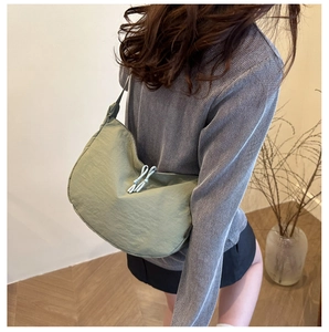 Detail of a light green crescent shoulder bag in nylon fabric on a model in a minimal room