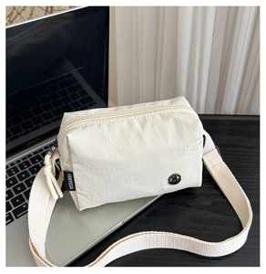 Détail d'un sac à bandoulière en nylon avec logo métallique et sangle large sur un bureau