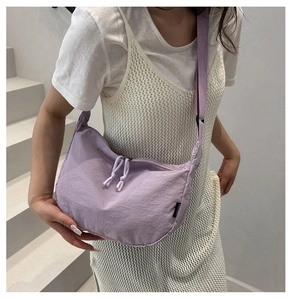 Model wearing a purple crescent nylon shoulder bag on a modern minimalist staircase