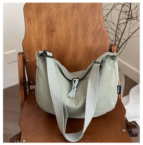 Detail of bean green crescent bag with tassel zipper and canvas texture on wooden chair
