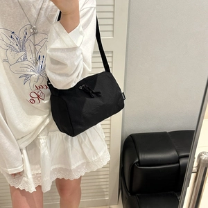Large black cylindrical nylon shoulder bag for women worn by model in minimalist setting