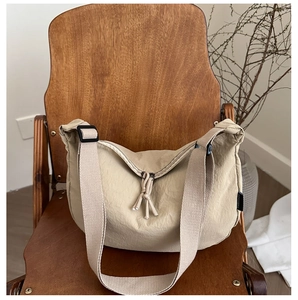 Close-up of khaki nylon crossbody bag with knot zipper on a wooden chair