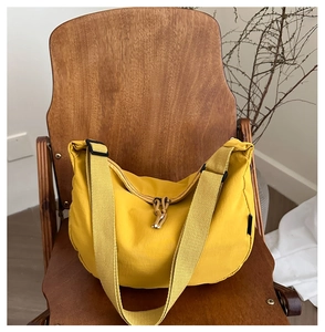 Detail of a bright yellow nylon crescent crossbody bag on a wooden chair with texture