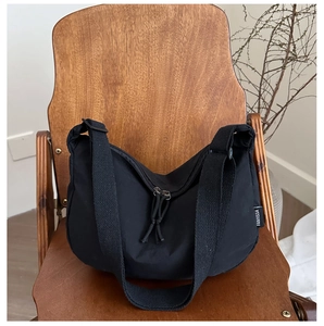 Close-up of black half-moon shoulder bag with dual zippers on a vintage wooden chair