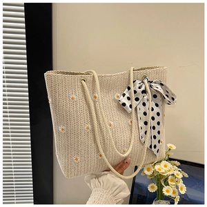 Dettaglio della borsa tote in paglia beige con ricamo a margherita e nastro a pois