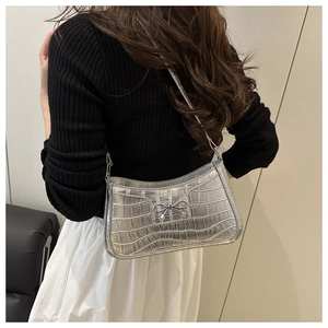 Detail of silver crocodile-embossed underarm bag with a metallic bow on the strap