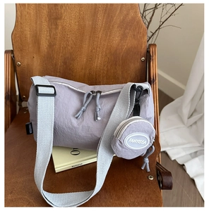 Detail of light grey nylon tote bag with wide strap and round coin pouch on a chair