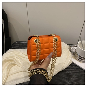 Close-up of bright orange quilted bag featuring a gold chain strap and square pattern