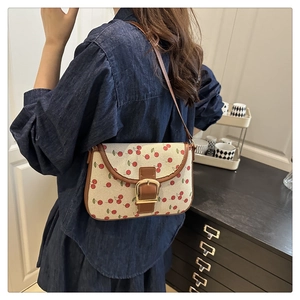 Detail of canvas shoulder bag with cherry print, brown leather trim and golden buckle