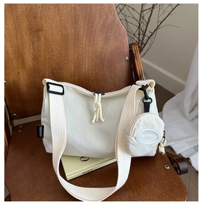 Detail of off-white tote bag with small round coin purse and wide strap on wooden chair