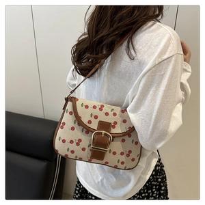 Detail of cherry print canvas handbag with brown leather trim and gold buckle accent