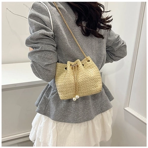 Straw bucket bag with gold chain strap and pearl drawstring detail on female model