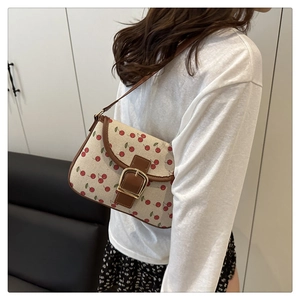 Detail of canvas cherry print handbag with brown trim and golden buckle on model
