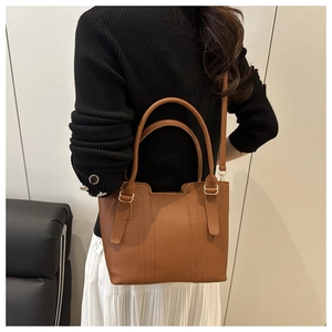 Detail view of brown pebbled leather tote bag worn by model in a stylish interior setting