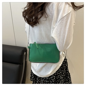 Detail of green crocodile texture cross-body bag with silver studs and chain strap